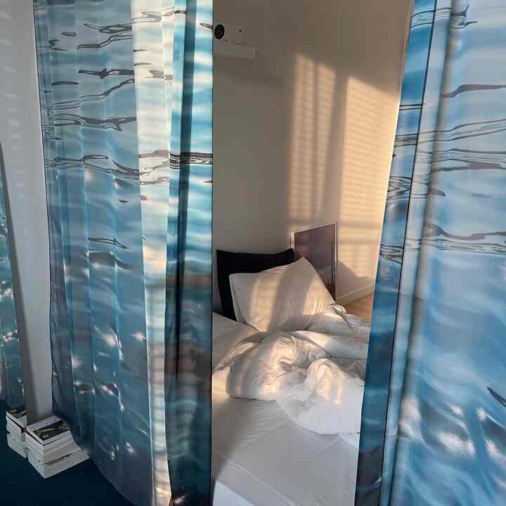 Cozy bedroom space featuring blue patterned curtains and white bedding illuminated by natural light
