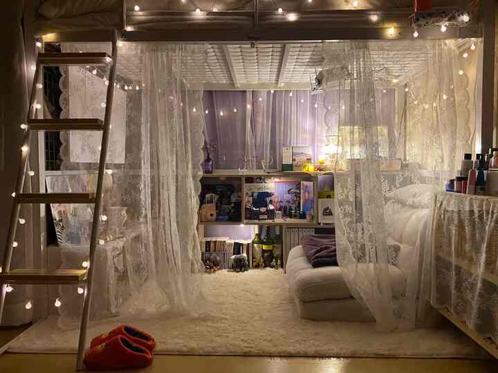 Cozy single household bedroom with warm lighting, lace curtains, a loft bed, and soft rug creating an inviting atmosphere