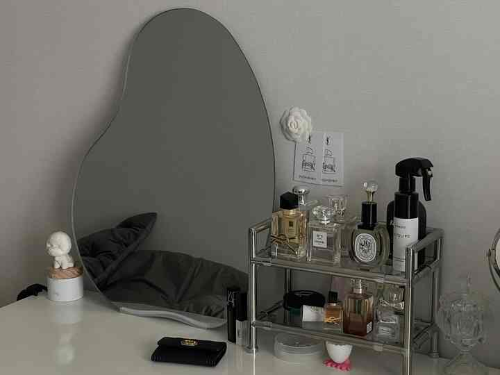 白とグレーのトーンの化粧台空間、特徴的な曲線形の鏡と香水ディスプレイが配されたモダンで洗練されたインテリア