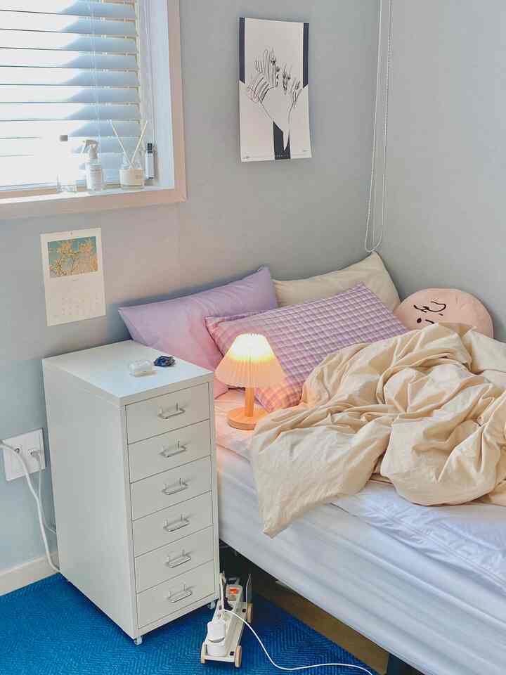 Cozy square studio bedroom with light sky blue wallpaper, white nightstand, pillows, and beige duvet cover
