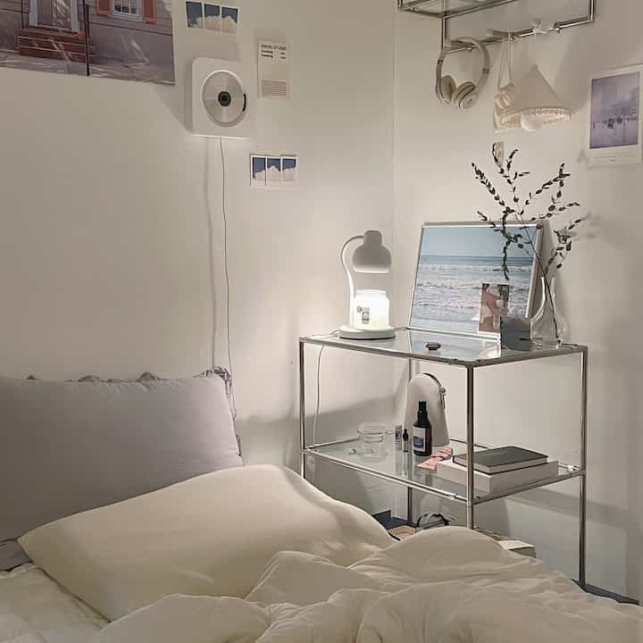 Natural white-toned single household bedroom featuring a stainless steel 3-tier shelf and posters, showcasing a minimalist space