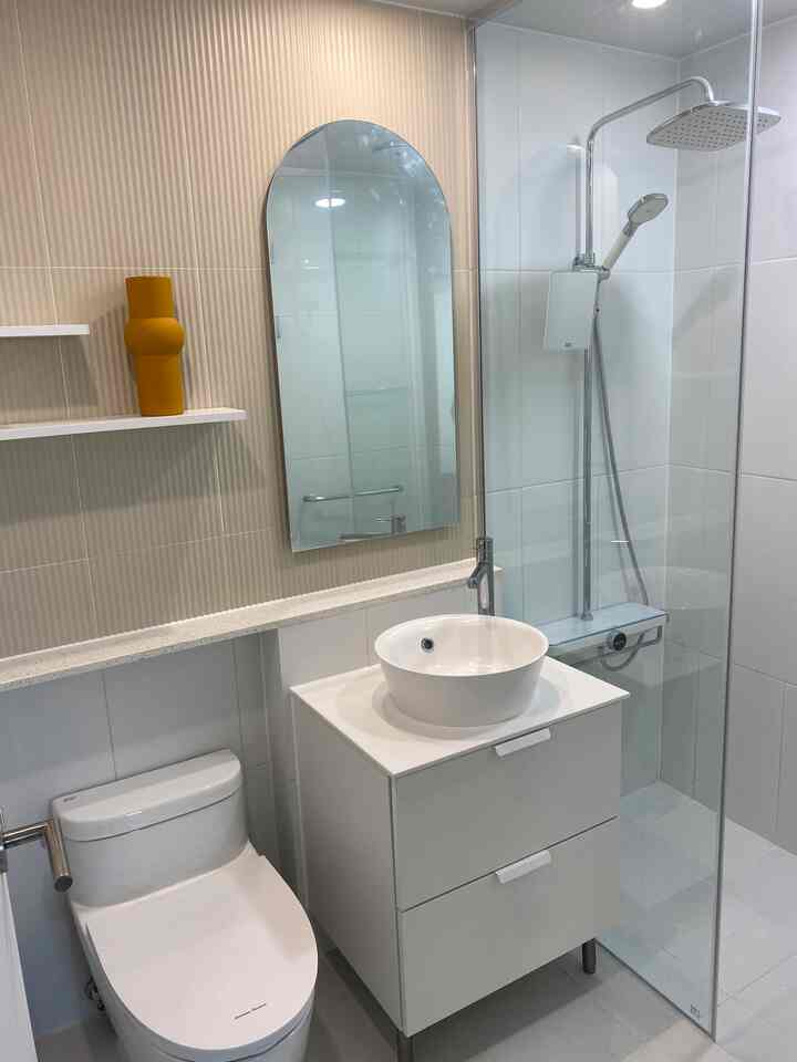 White-toned bathroom with Tembaboard style tiled wall, arched mirror, vanity cabinet with vessel sink, and glass shower enclosure creating a modern space