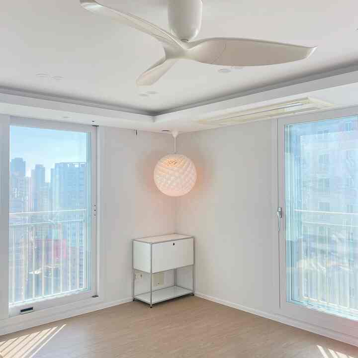 白い壁と天井、木目調の床、ペンダントライトとシーリングファンがあるシンプルなリビング