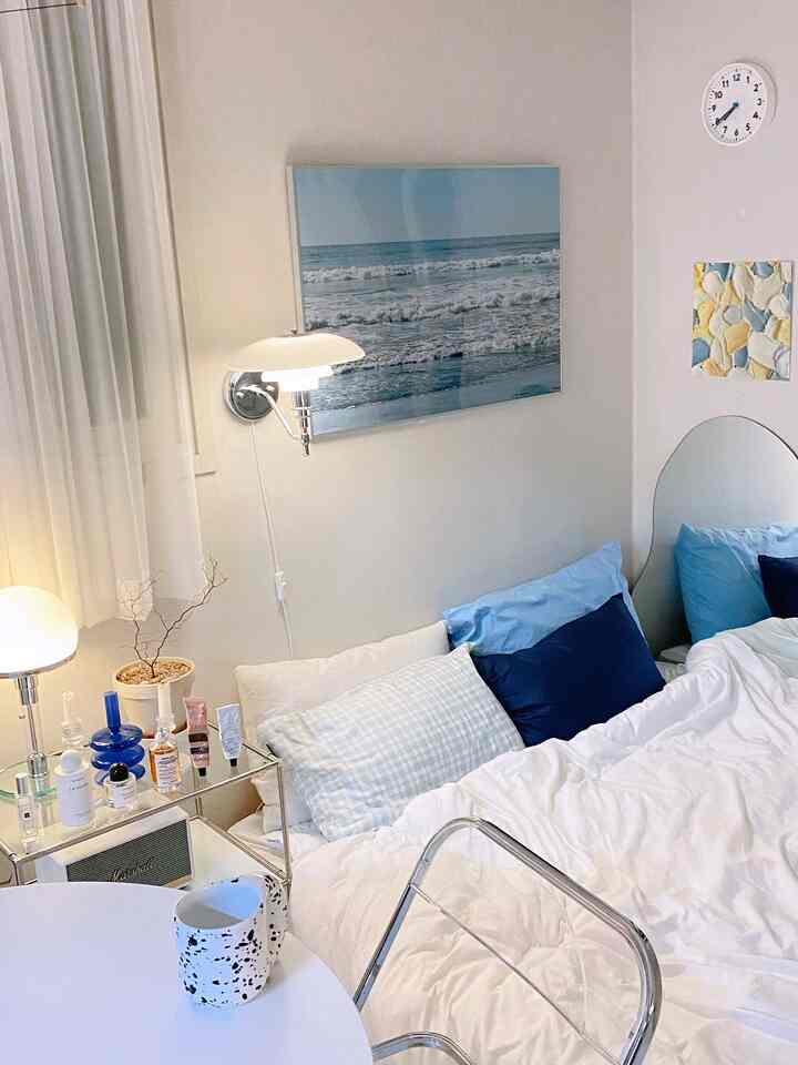 White and blue toned bedroom featuring transparent chair, wall sconce, bedding, and pillow covers in a fresh, clean setting