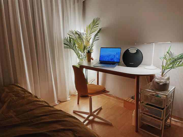 Natural tone studio bedroom with white curtains, minimalist desk and office chair featuring a cozy home office setup