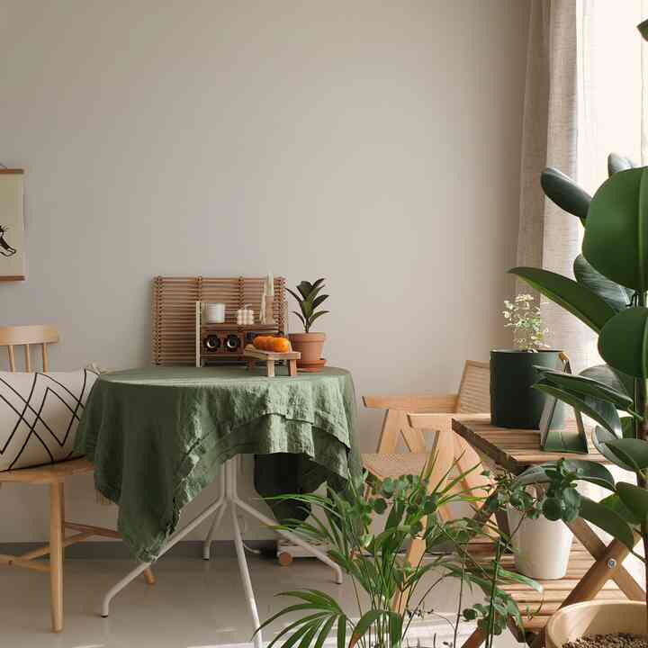 ナチュラルな色調のダイニング、グリーンのテーブルクロスをかけた円形テーブルと木製の椅子、植物が配置された雰囲気のあるインテリア