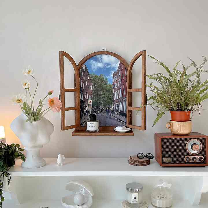 Cozy decorative space with a white wall background featuring a wood-toned window frame art piece and plants centrally placed