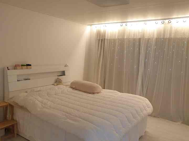 Warm ivory-toned bedroom featuring a white bed with pillows centered, sheer lace curtains creating a cozy ambiance