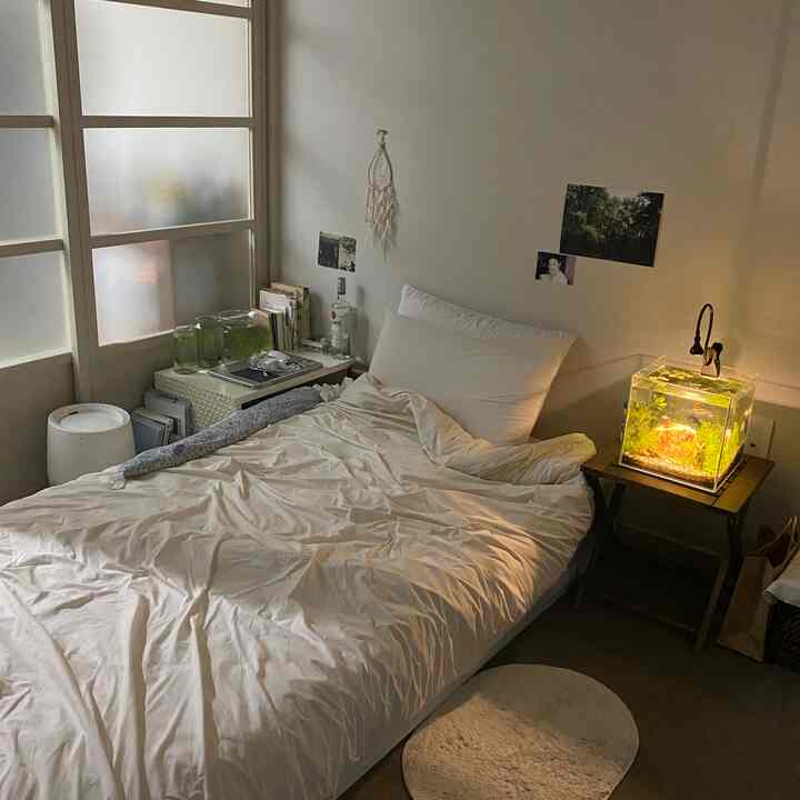 柔らかいアイボリー色調の寝室、中央に掛け布団カバーがあるベッドと右側に水槽が配置された温かみのある空間