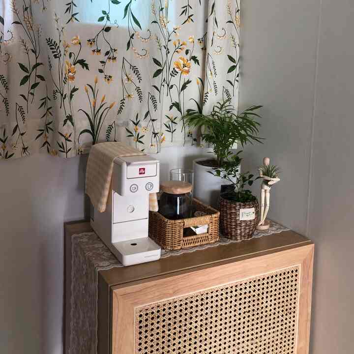 ナチュラルなライトブラウンの木製キッチンキャビネットにコーヒーマシンと観葉植物が配置された、落ち着いた印象のホームカフェ空間