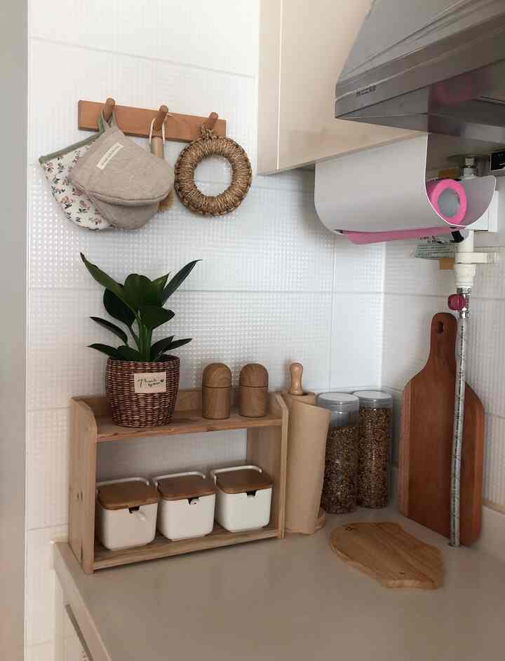 White tiled backsplash kitchen with wood-tone shelves featuring seasoning jars, cutting boards, and a plant in a neat arrangement