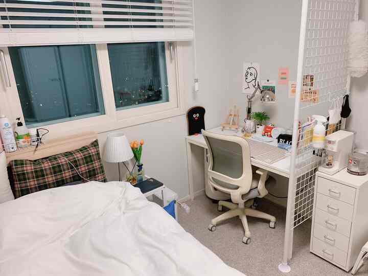 Bright white-toned bedroom space featuring a desk with office chair by the window, creating a cozy single-room atmosphere