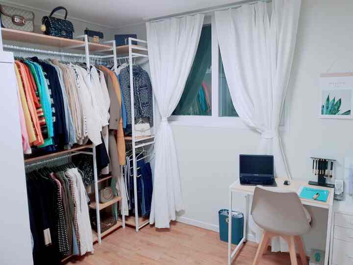 White and wood tone walk-in closet featuring open storage racks and a desk, creating a neat and simple space