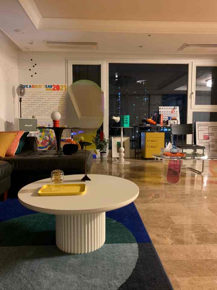 Modern living room with natural wood flooring, white round table, and colorful decorative items arranged