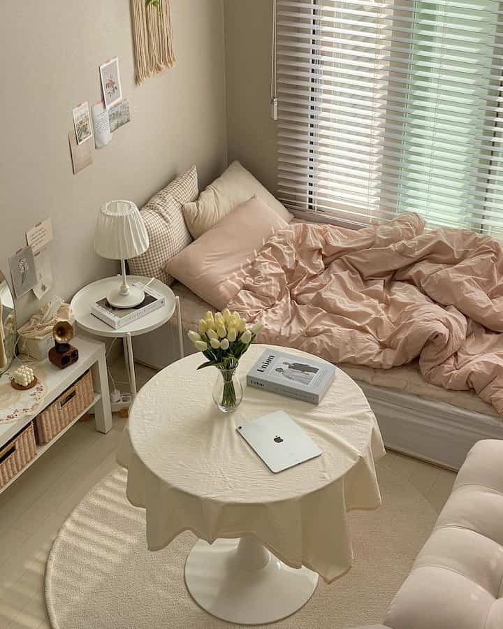 Beige and white toned studio bedroom featuring a cozy bed and round table with a natural atmosphere