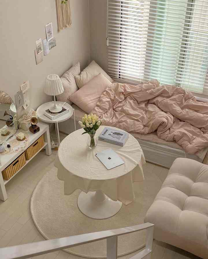 A natural-toned studio living-bedroom with white and beige hues, featuring a round rug, round table, and comfortable sofa