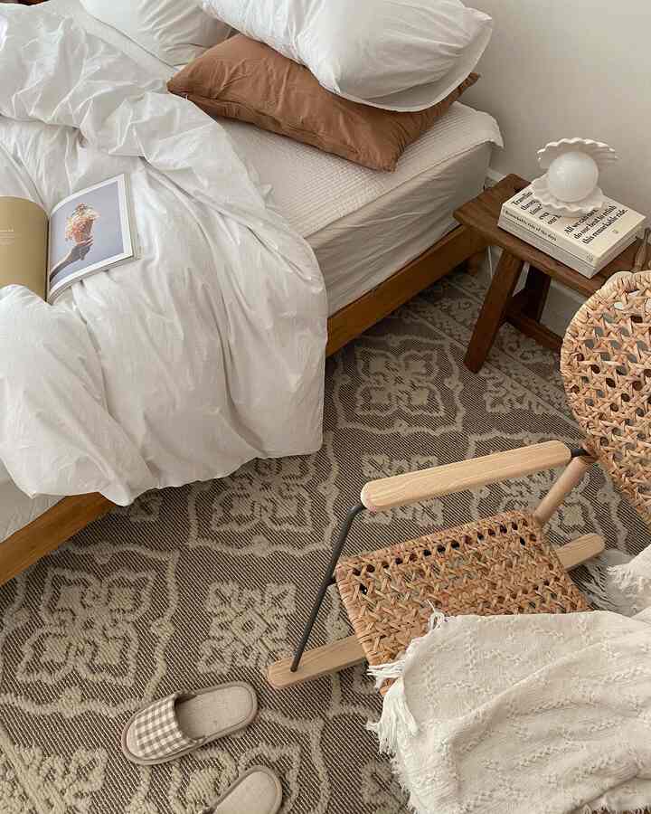 Beige and monotone bedroom featuring wooden bed, patterned rug, and rattan armchair creating a cozy natural atmosphere