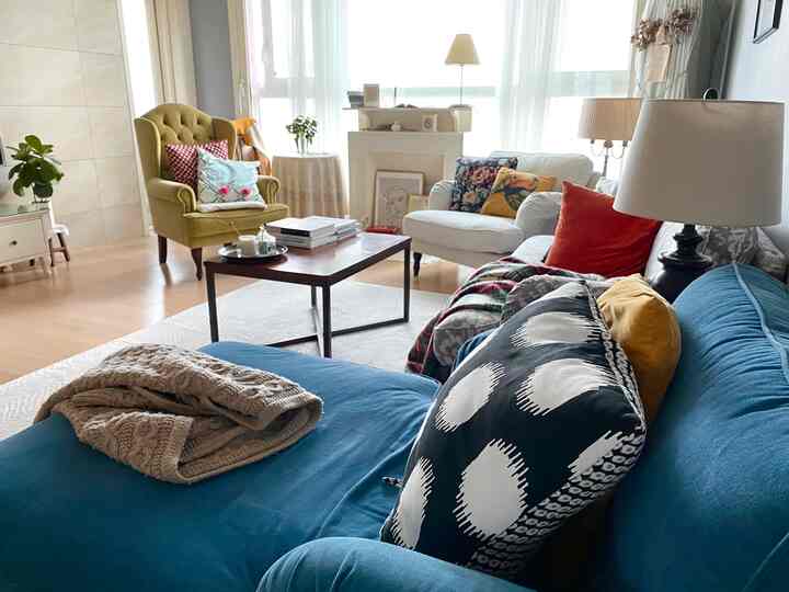 ブルー、ホワイト、グリーンのトーンのリビングルーム、ソファとアームチェア、コーヒーテーブル、額縁や暖炉が配置された雰囲気のあるインテリア