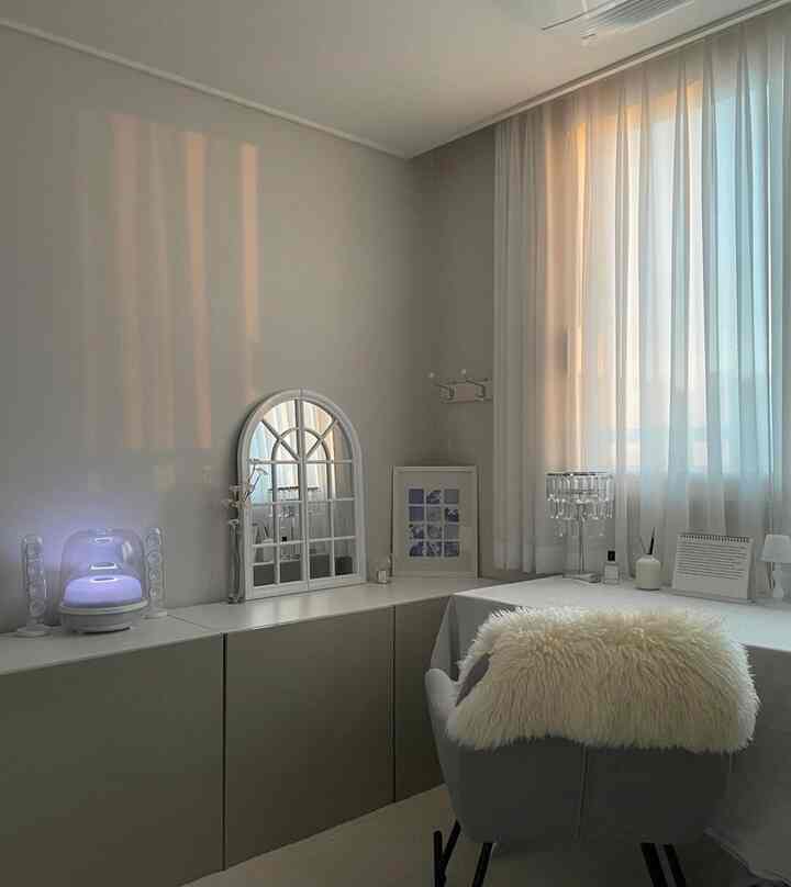 A cozy study in soft white and gray tones with window draped in sheer curtains, featuring a mirror and a desk