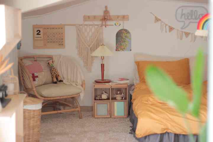 温かみのあるナチュラルな木目調のロフト寝室、ミニ収納キャビネットとラタンチェアが配置された雰囲気のあるインテリア