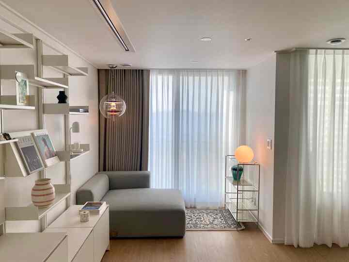 White-toned bedroom mini study featuring a gray sectional sofa, wall shelves, and ambient lighting with a clean, cozy atmosphere