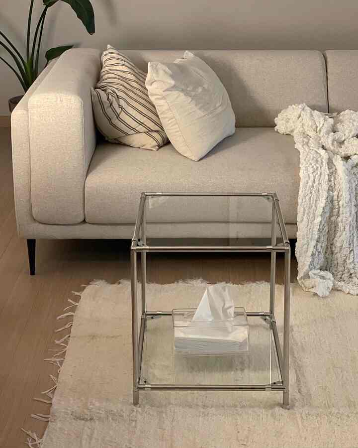 Beige and ivory toned living room featuring beige sofa with striped and plain cushions, chunky knit blanket, stainless steel side table, and ivory rug in a natural modern style