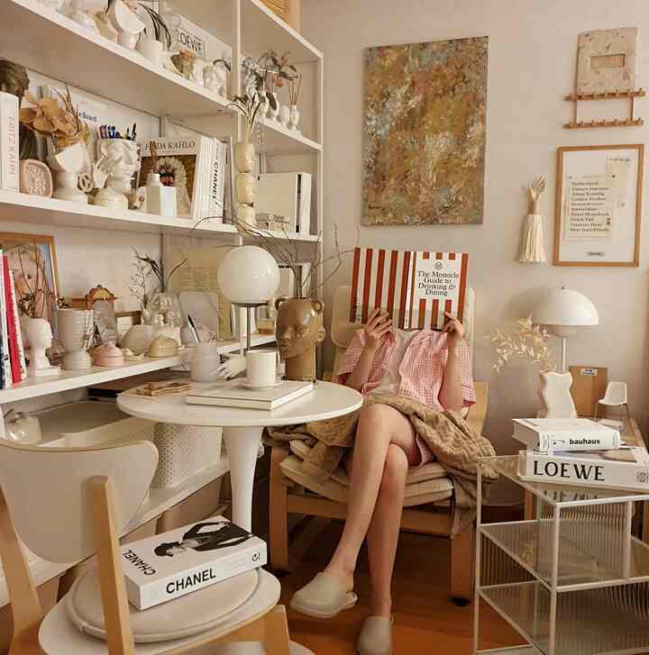 Beige and white toned mini library and home cafe space featuring round table, armchair, and bookshelf with cozy decor