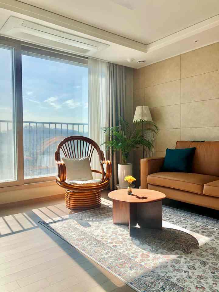 自然な木目調と陽光が差し込むリビング、ラタンのアームチェアとブラウンのソファが配置された温かみのあるインテリア