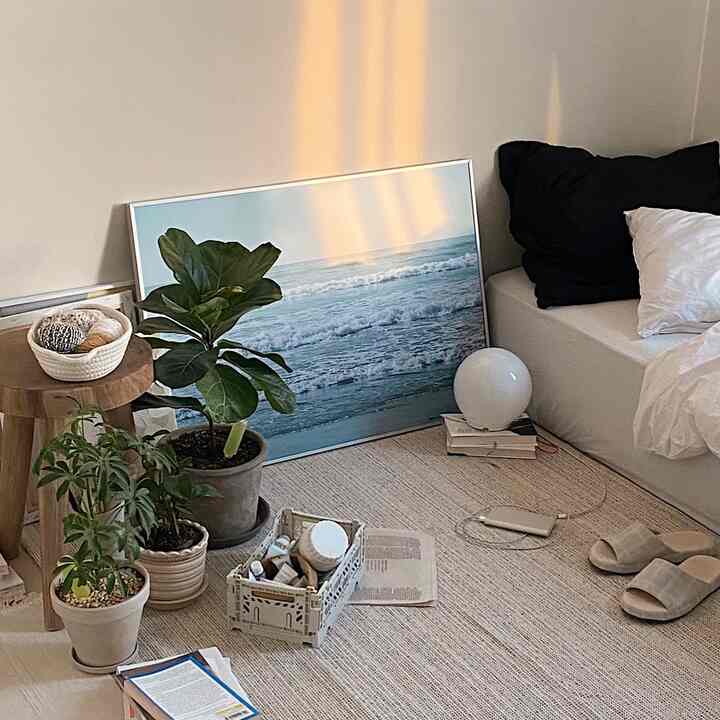 Natural tone bedroom corner featuring plants, large ocean poster, wooden stool, and light sofa creating cozy atmosphere