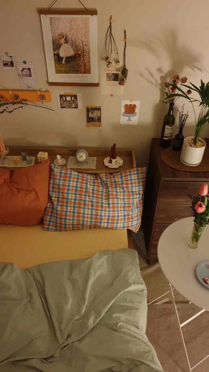 Warm brown and beige toned small bedroom featuring a bed, wooden storage cabinet, art poster, and candles creating a cozy atmosphere