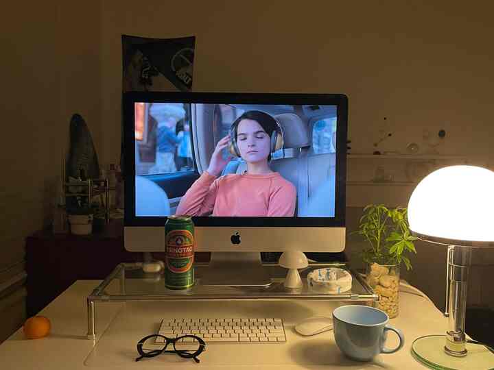 Cozy lit studio home office with transparent acrylic monitor stand, iMac, and assorted desktop accessories on desk