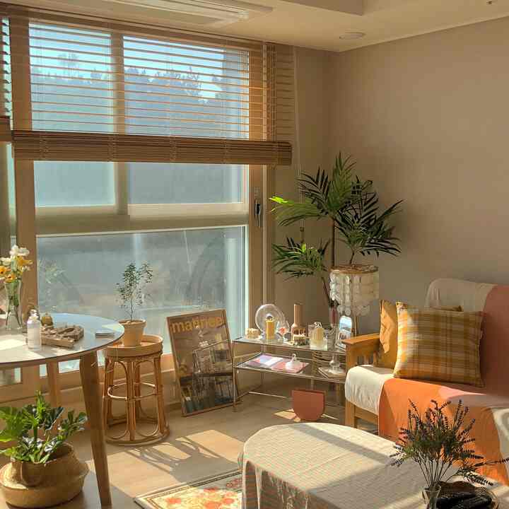 明るいナチュラルな木目調とベージュ色調のリビング、丸テーブルとソファ、モジュール棚、多様な小物が温かな陽射しの中に配置された空間