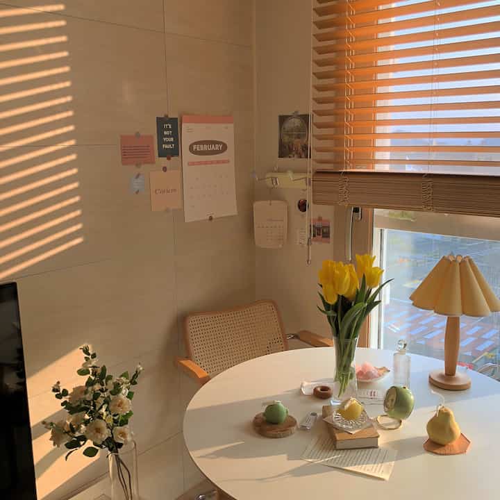 ナチュラルな木目調とベージュの壁のダイニングルーム、丸テーブルの上に黄色いチューリップの花瓶と様々なキャンドルが置かれた温かみのある空間