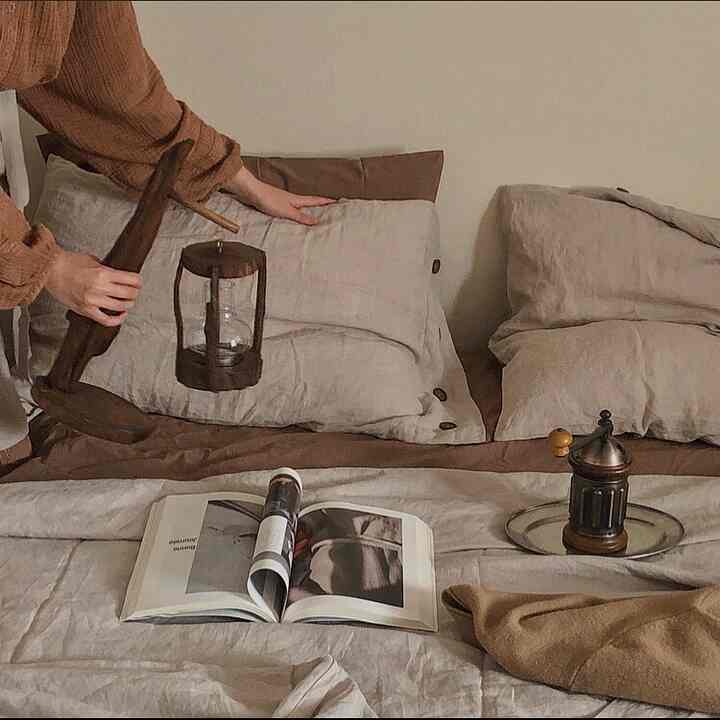 ベージュとブラウンの色調の寝室、リネンの寝具と木製オブジェが配置された雰囲気のあるインテリア