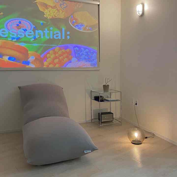 Natural-toned living room featuring a gray bean bag centrally placed, with a glass side table and table lamp on the right, presenting a modern and calm atmosphere