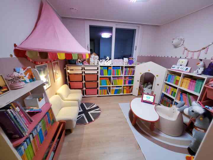 ピンクとベージュのトーンが調和した子供部屋の読書空間、子供用ソファと本棚が配置された雰囲気のあるインテリア
