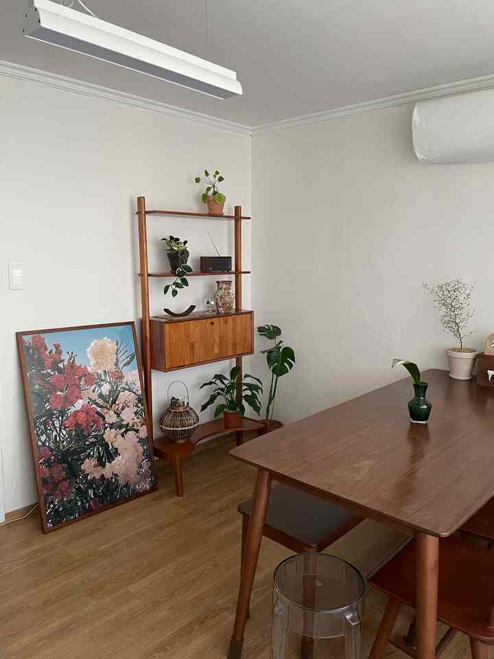 暖かい木目調と白い壁のダイニング、木製のダイニングテーブルとベンチ、透明なスツール、植物が配置されたナチュラルでシンプルなインテリア