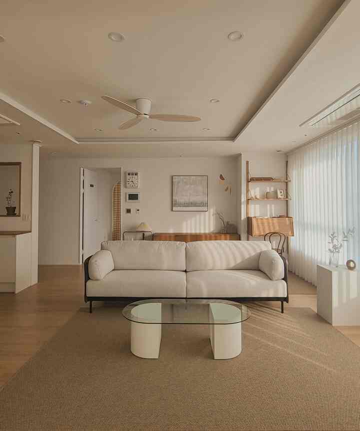 Bright white and wood tones blend in a simple and natural living room featuring an ivory sofa and transparent glass coffee table centrally placed