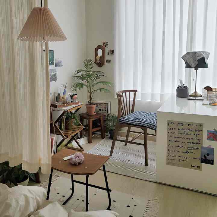 A small studio apartment featuring white curtains, wooden chair, and indoor plants with a natural decor style