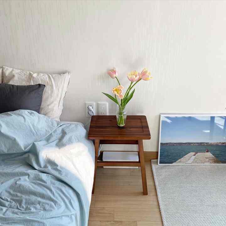 Light brown small bedroom with wooden stool displaying a vase of pink tulips in a simple setting