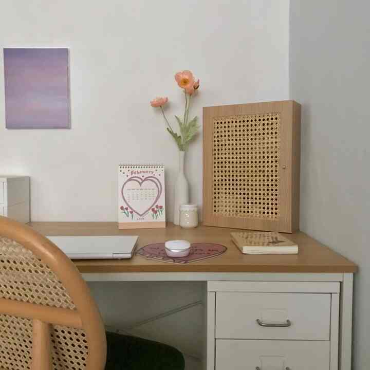 Natural color and white toned desk featuring rattan chair and vase with flowers in a cozy home office space
