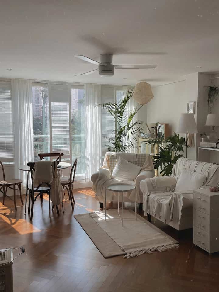 A bright living room in white and brown tones featuring herringbone flooring, wooden dining chairs, and an armchair creating a natural ambiance