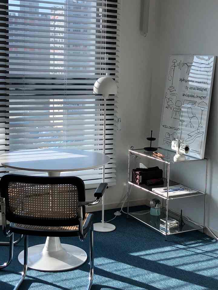 白い壁とネイビーのラグがあるホームオフィス、丸テーブルとアームチェア、メタル棚とフロアランプが配置された落ち着いた印象の空間