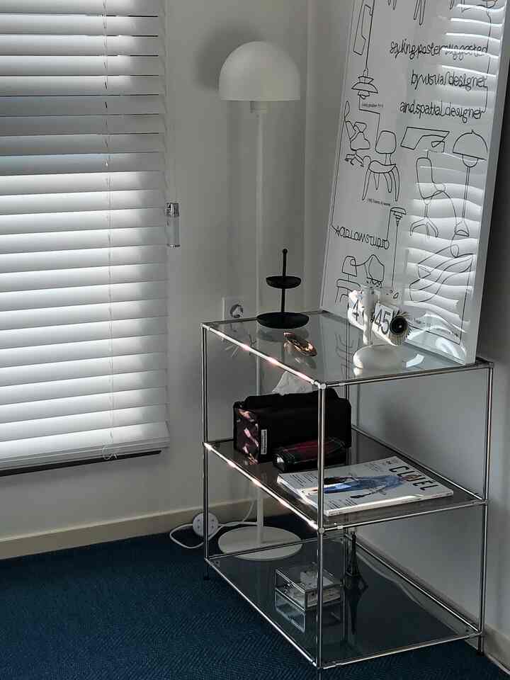 ホワイトブラインドと透明なメタルサイドテーブル、ネイビーラグがあるモダンなリビングの一角