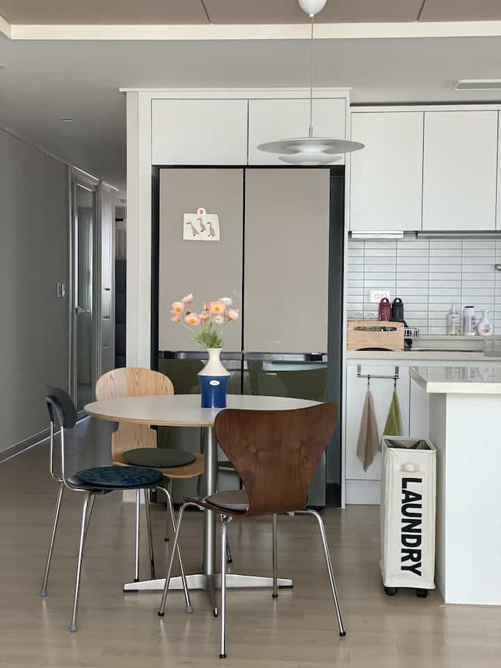 A white and brown toned kitchen and dining space featuring a round table with various chairs in a cozy modern natural interior