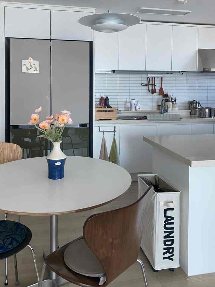 ナチュラルな色調のキッチンスペース、丸いダイニングテーブルと木製チェア、造花のケシの花が置かれた清潔感のあるインテリア