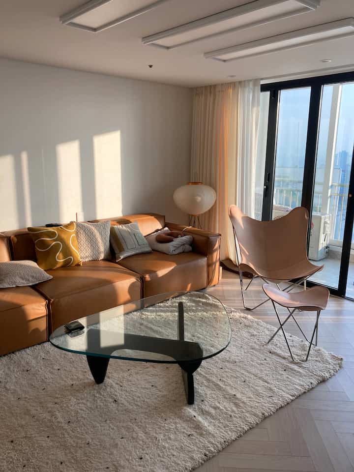 Warm natural tone living room featuring leather sofa, butterfly chair, and glass coffee table with cozy atmosphere