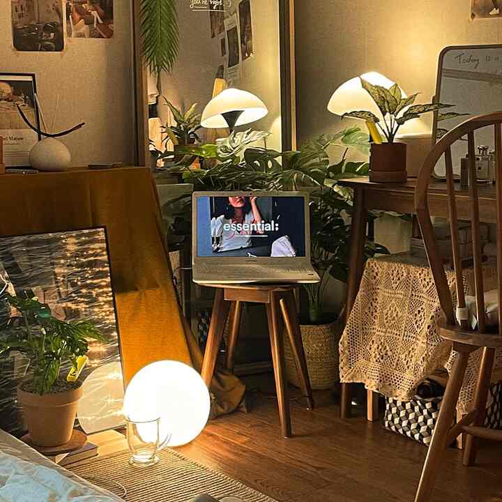 Cozy room with warm wood tones and lush green plants, featuring table lamps and stool forming a home office vibe