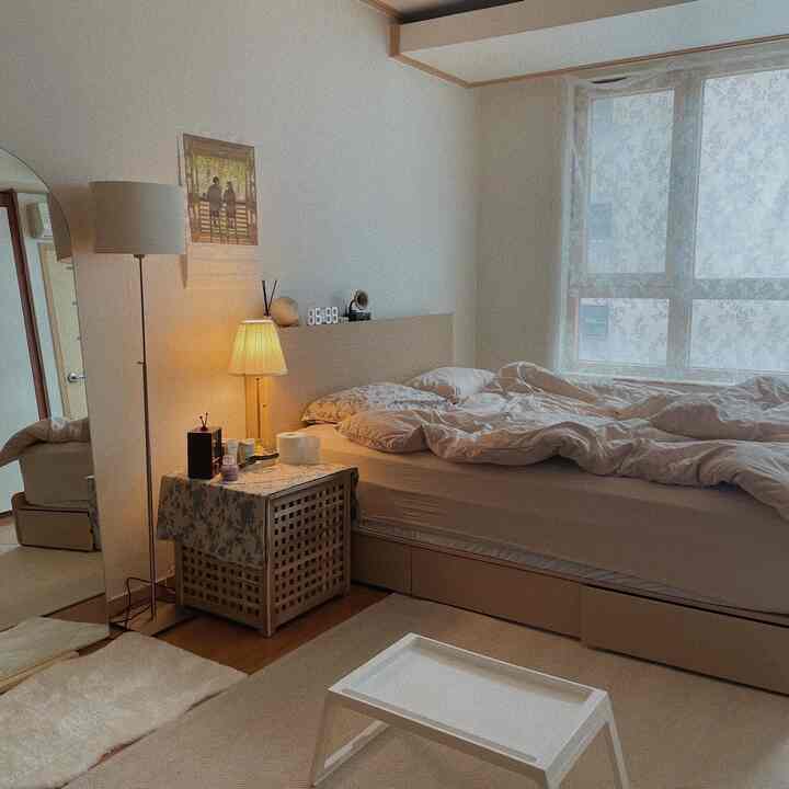 Beige-toned studio bedroom featuring a cozy bed and floor lamp with a warm atmosphere