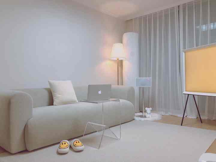 白を基調とした狭いリビング、シンプルなソファと透明なテーブル、フロアランプが配置された清潔感のある空間